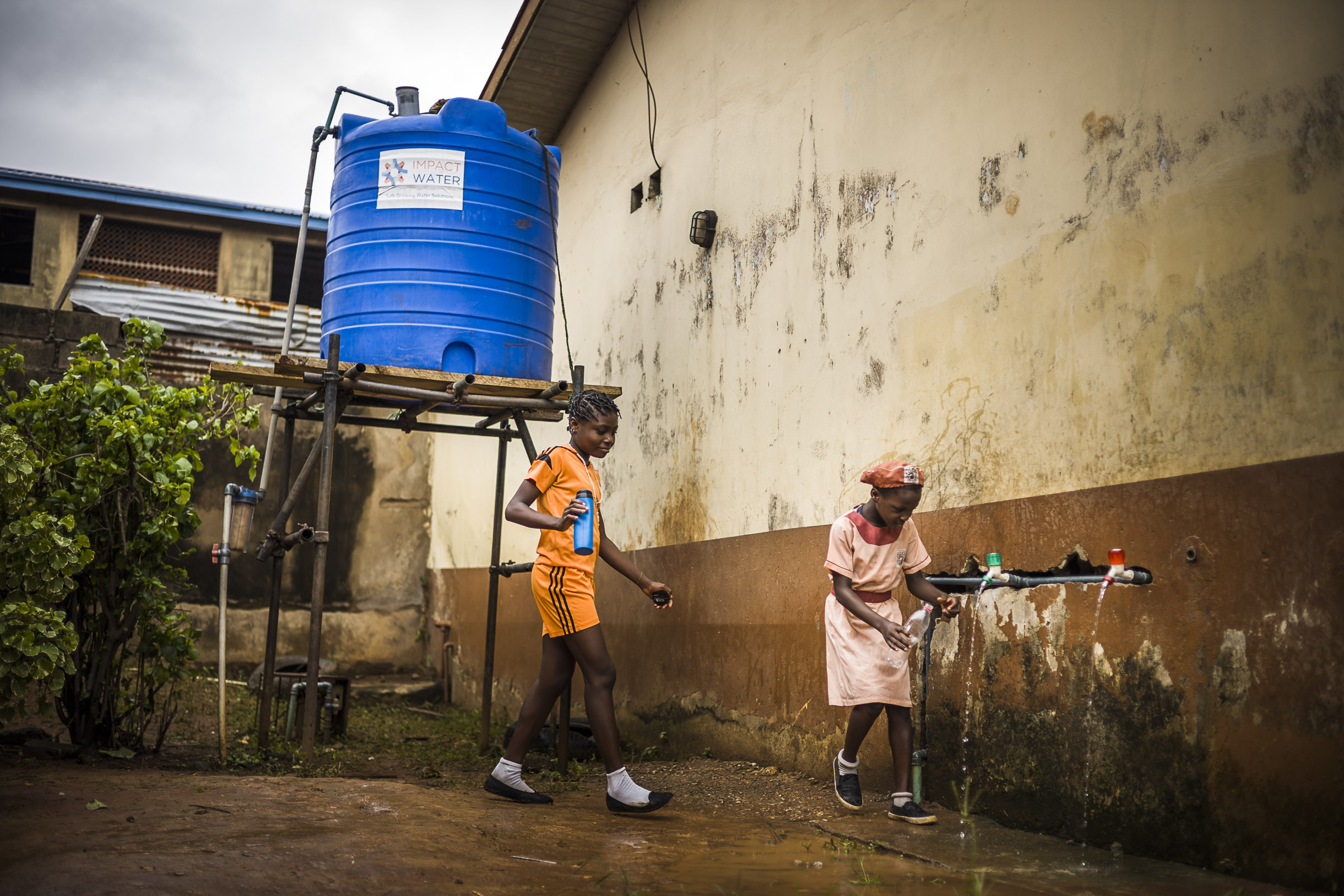 Zwei afrikanische Kinder, die sich über das Wasser freuen und ihre Wasserflaschen aus dem neuen Wasserhahn auffüllen.